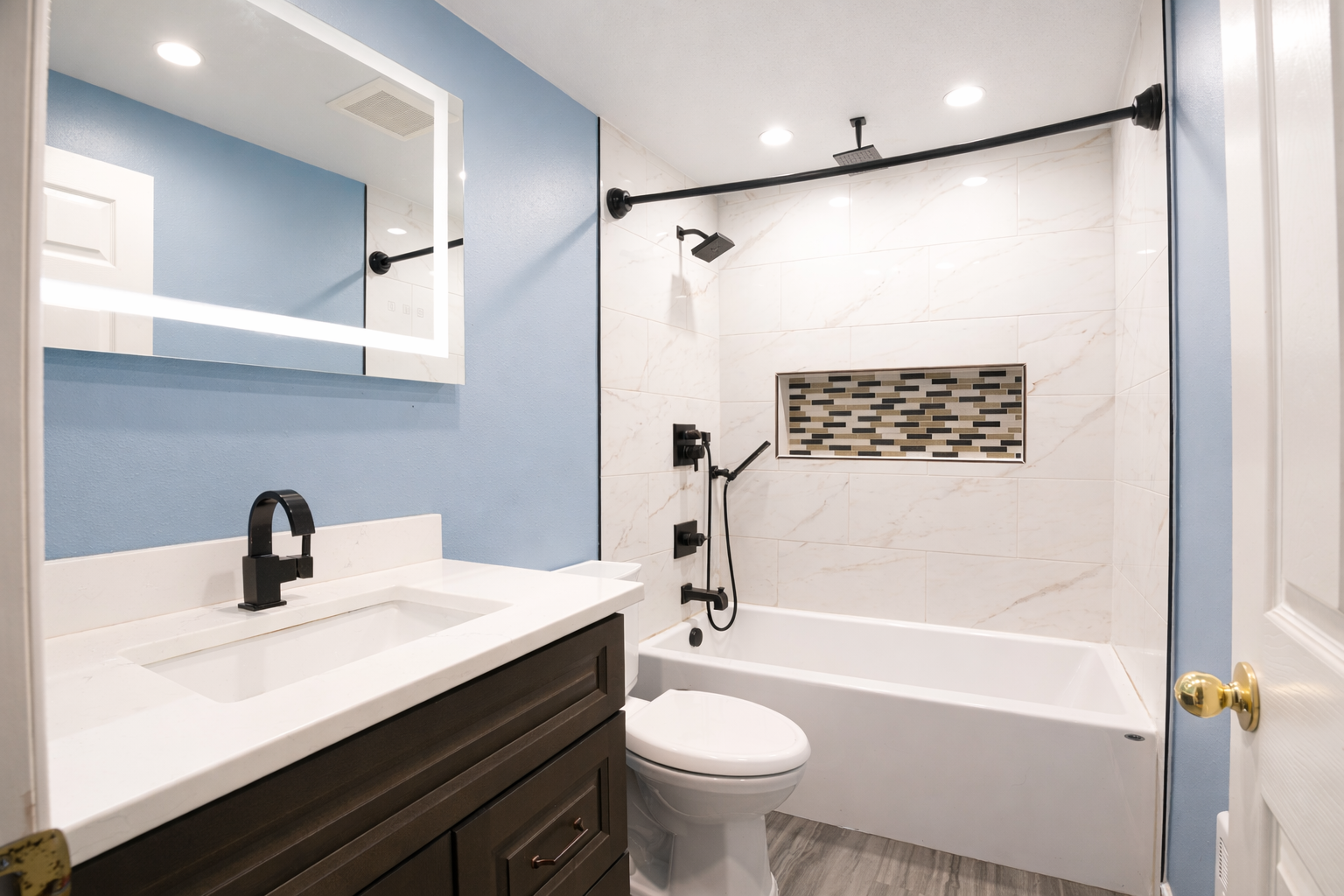 Remodeled bathroom with dark vanity and tiled tub surround